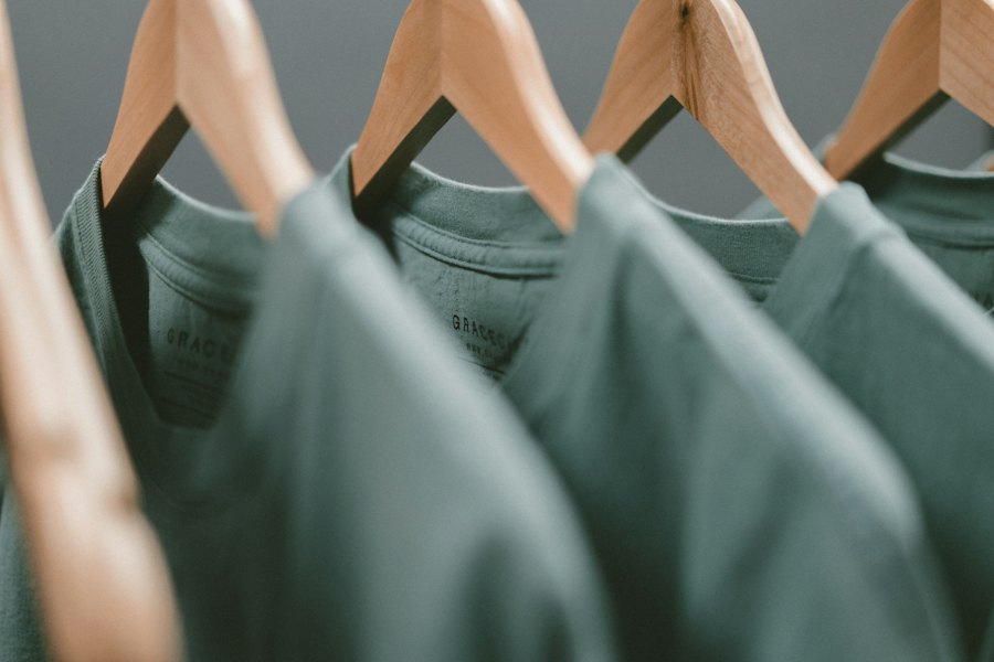 Sage green crew-neck cotton tees on wooden hangers