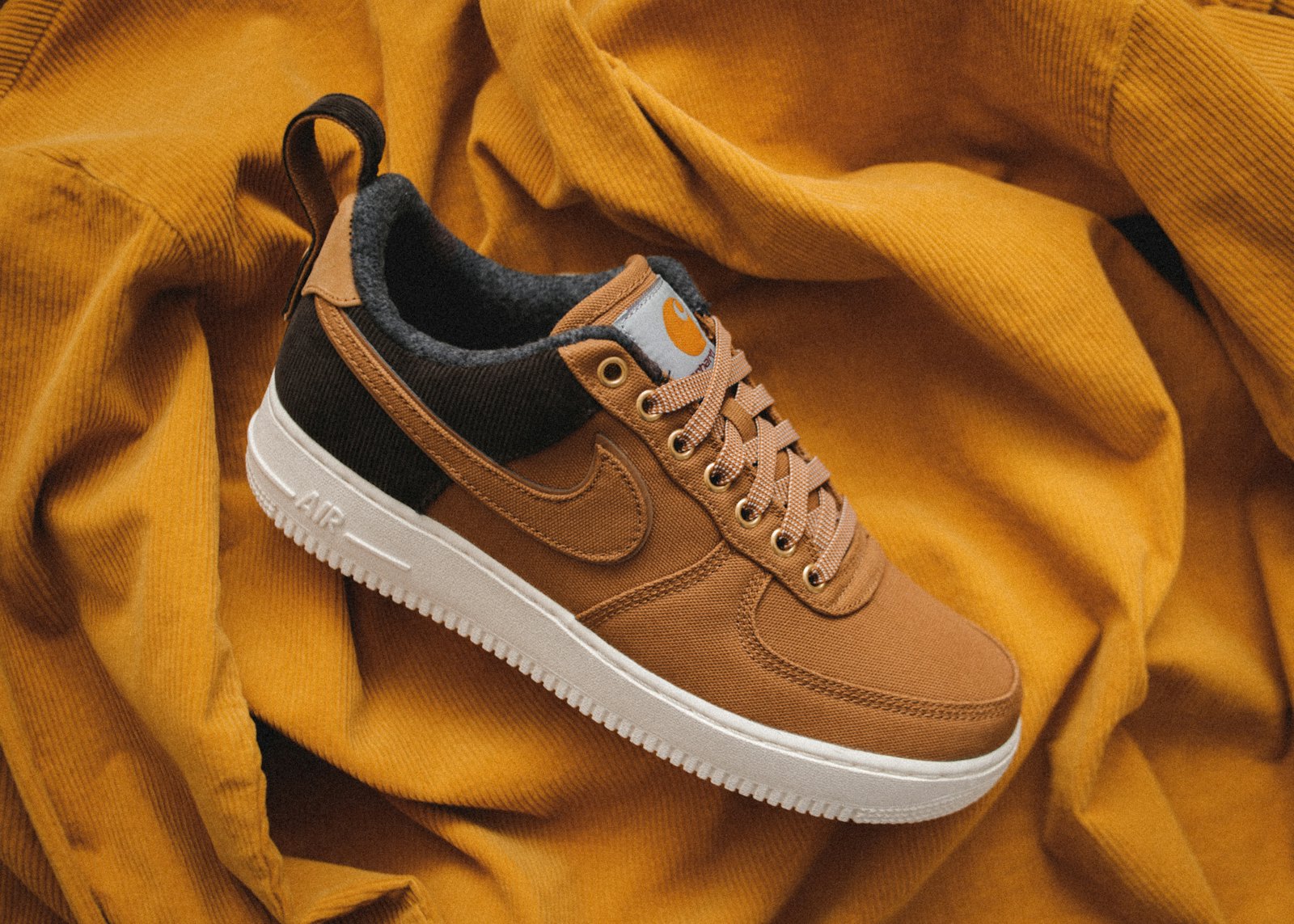 Tan canvas sneaker with a dark brown collar and chunky off-white sole, resting on mustard corduroy