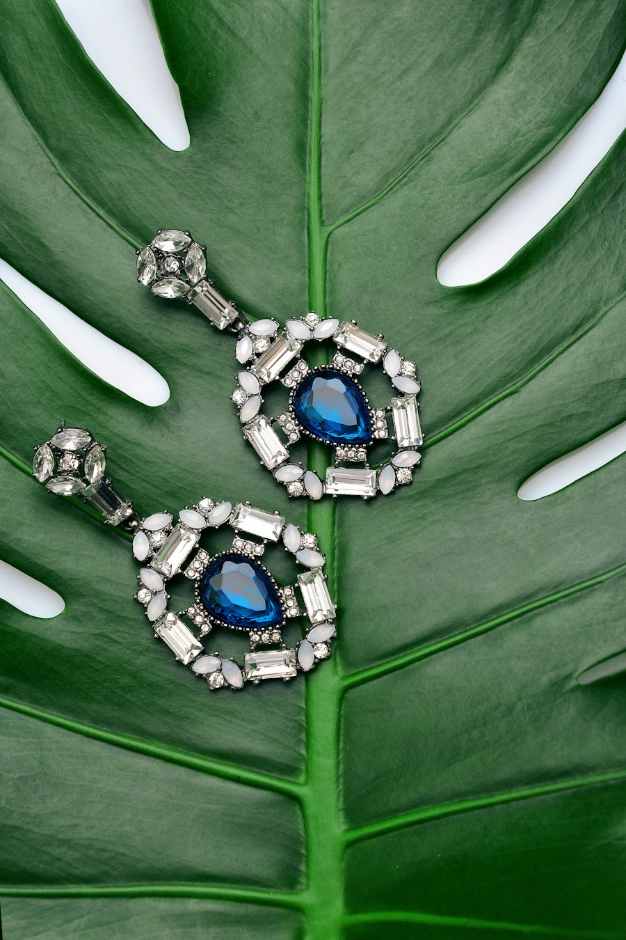Drop earrings with deep blue stones on a green leaf