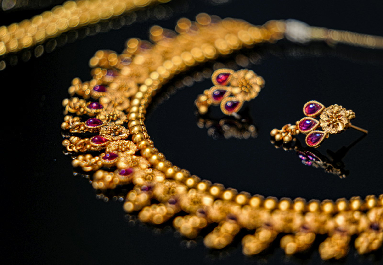 Antique-finish 22K gold necklace with ruby-red drops and matching earrings on black