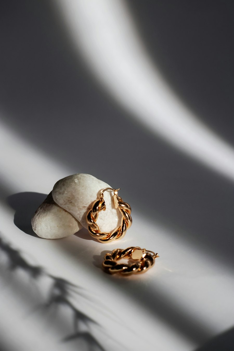 Small twisted gold hoop earrings on a white stone