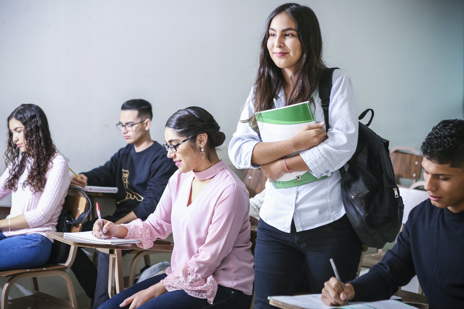 A smiling student holding her notebook in class while classmates write at their desks